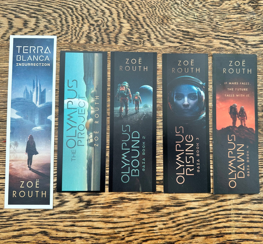 Five bookmarks from covers of the Zoe Routh and Terra Blanca author series arranged in a row on a wooden tabletop. The books include Insurrection, The Olympus Project, Olympus Bound, Olympus Rising, and Olympus Dawn.