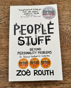 The front cover of the book 'People Stuff: Beyond Personality Problems' by Zoë Routh, displayed flat on a brown wooden surface. The cover is white with bold black typography and small stick-figure illustrations, featuring gold Business Book Awards seals.